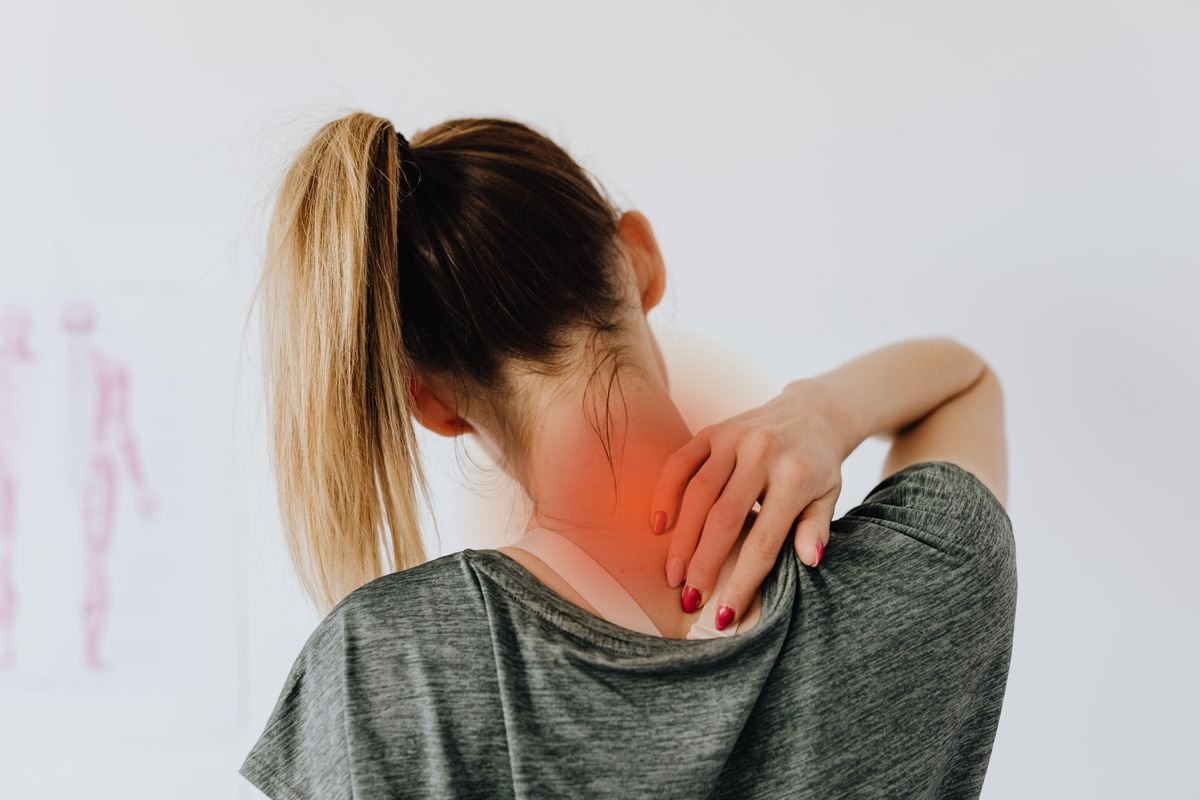 Mujer de espaldas con dolor muscular en cuello y hombro, zona de dolor resaltada